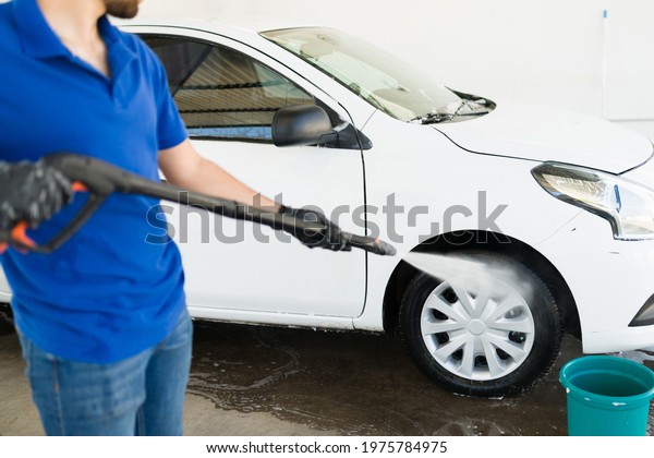 Hardworking young man using a pressurized water hose.\
Latin worker cleaning the tires of a vehicle at his job at the car\
wash 