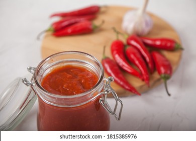 Harissa In A Glass Jar Close-up And Hot Chili Peppers On A White Background