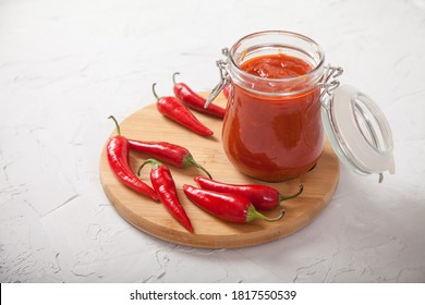 Harissa In A Glass Jar On A Wooden Stand And Hot Chili Peppers On A White Background