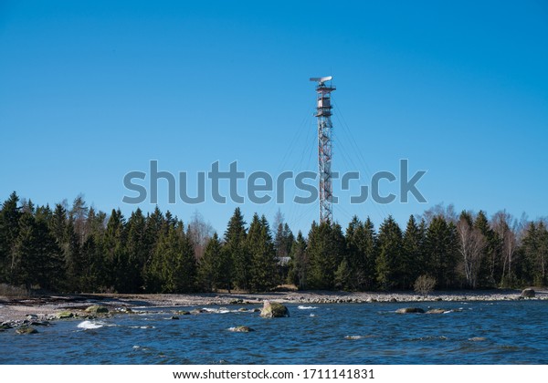 Harjumaa/Estonia-04.17.2020: Mobile tower in fenced\
area. Amazing blue sunny sky on the background, 4G, 5G Radio tower.\
Cell data mast. Communication tower on Lumida peninsula. Television\
signal\
tower
