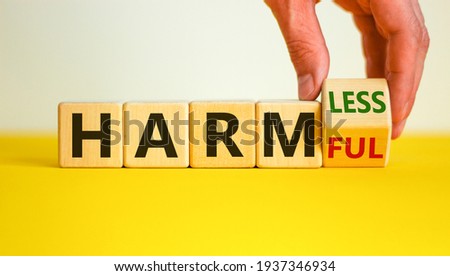 From harmful to harmless. Male hand turns the cube and changes word 'harmful' to 'harmless'. Beautiful yellow table, white background. Business and harmful or harmless concept. Copy space.