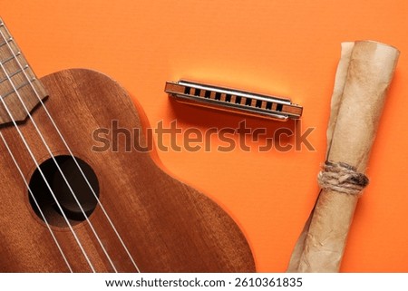 Harmonica, ukulele and scroll on color background, closeup