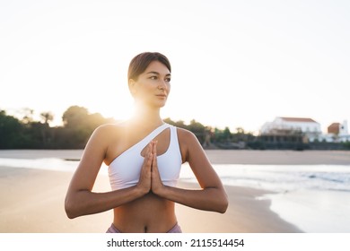Harmony and meditation training during morning yoga at coastline beach, contemplative female in sportswear praying in namaste pose during aerobic pilates for exercising own body concentration in asana