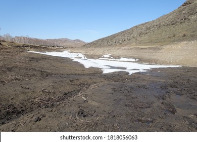 Harsh nature landscape and road through fields and mountains along the riverbed for off-road SUV with puddles and mud. Spring background with wet earth and snow and slush