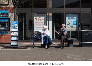 Hartlepool / Great Britain - April 20, 2019 : Elderly Couple Sit On A Bench Beside Jehovahs Witness Stand Talking And Discussing.