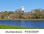 Harvard University in early spring. Green dome of Eliot House against clear blue sky, a rowboat in Charles River, people walking in the background. Beautiful college campus scenic.