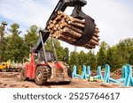 Harvester log loader working in plant manufacturing yard outdoors. Sawmill for treatment and processing of pine wood in factory with lumber. Woodworking industry, logging concept. Copy ad text space