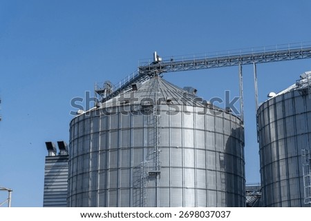 Harvesting facility features large grain silos with a clear blue sky in the background during midday, showcasing agricultural storage