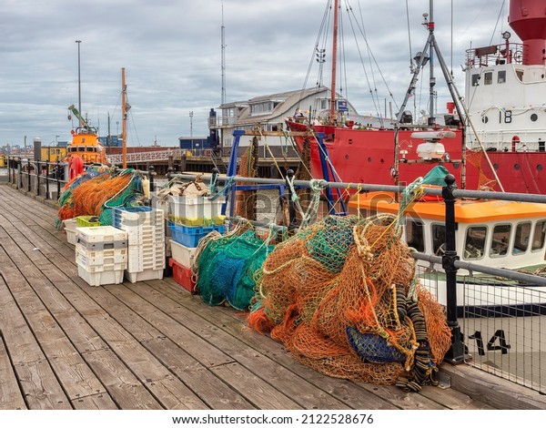 HARWICH, ESSEX, UK - AUGUST 12, 2018:  View of\
the harbour with nets and crates on the quay with fishing trawlers\
in the background