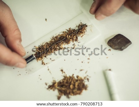 Hashish set. Man preparing hashish joint rolling marijuana cigarette for smoking. Close up