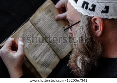 A Hasidic Jew reads Siddur. Religious orthodox Jew with a red beard and with pace in a white crocheted bale praying. Closeup