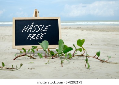 HASSLE FREE. Chalkboard with written message and beautiful beach background.