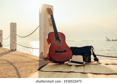 Hat, Bag And Guitar On Reed Mat Near The Sea At Sunset. Travel, Vocation, Holiday, Summer Concept.