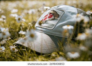 Hat featuring pizza design placed on grassy field with blooming wildflowers surrounding