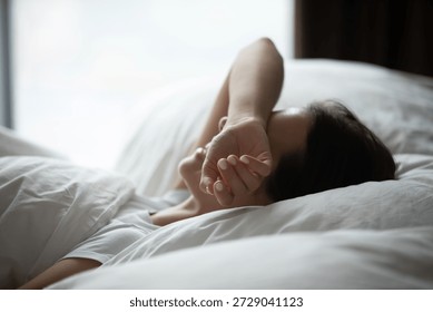 I hate waking up early. Side view sleepy lazy young woman lying in comfortable bed hide closed eyes beneath arm avoid morning sun pretend nap protect herself from daylight wish to prolong sweet sleep