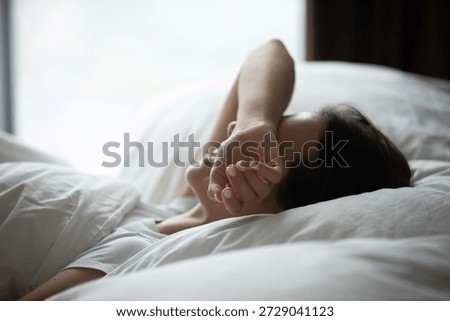 I hate waking up early. Side view sleepy lazy young woman lying in comfortable bed hide closed eyes beneath arm avoid morning sun pretend nap protect herself from daylight wish to prolong sweet sleep