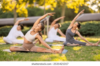 Hatha yoga coach conduct leading rehearsal for girls and guys in park, show example of performing exercises, do fulfil Parivritta Janu Shirshasana. People practice sport during yoga workout in nature - Powered by Shutterstock