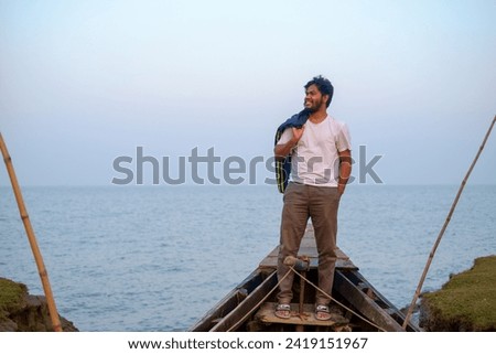 Hatiya,Bangladesh- December 29,2023:  Young Bangladeshi traveler sitting on a wooden fishing boat near a river 
