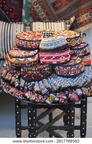 Hats with bright patterns sit stacked on a wooden chair in a market.