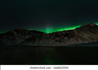 HAUKLANDBEACH, LOFOTEN / NORWAY– MARCH 07, 2019: A view at Hauklandbeach (near to village Leknes / Lofoten). huge northern lights is shining/glowing over the mountains with starry stars.