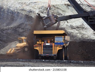 A haul truck is being loaded with dirt and ore at a mine site while another haul truck waits in the foreground.