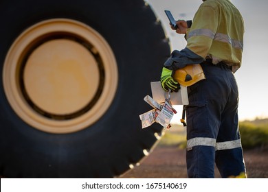 Haul Truck Inspector Wearing Work Uniform Safety Glove Holding Hard Hat Danger Tags Personal Locks Inspection Pre Operation Book Inspecting Taking Pic With Cell Phone Defocused Haul Truck Background