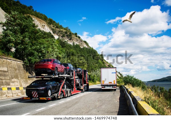 Hauling cars. Car carrier transporter truck on\
road. Auto vehicles hauler on driveway. New cars transportation.\
Hybrid and electric\
cars.