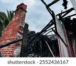 A haunting image of the Coastal Cottege in La Jolla, California, built in 1890, destroyed by fire, with charred remains and a lone brick chimney standing tall.