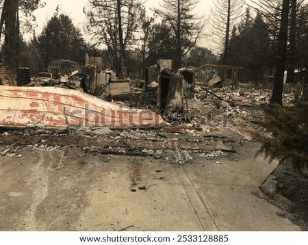 A haunting landscape of devastation after a wildfire, with charred remains of a vehicle, home, and personal belongings under a smoke-hazed sky.