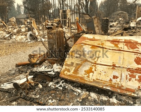 A haunting landscape of devastation after a wildfire, with charred remains of a vehicle, home, and personal belongings under a smoke-hazed sky.