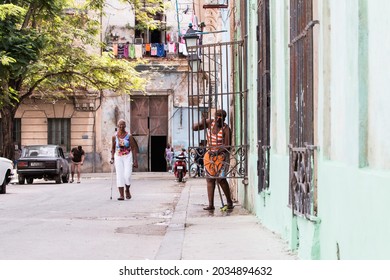 Havana, Cuba 3_31_2018  Urban Scene  With An African American Older Woman Cleaning The Porch Of Her House And Colorful Decaying Buildings In Old Havana