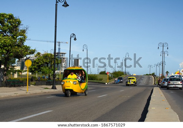 Havana,\
Cuba - August 27 2018: A coco motorcycle taxi comes with its\
passengers along the first street in Old\
Havana.