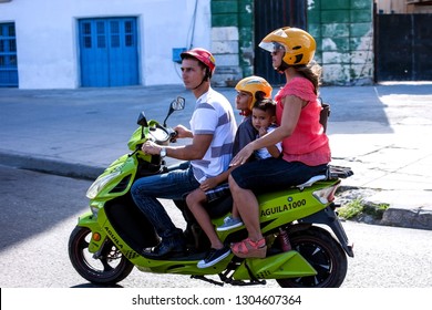 HAVANA, CUBA - DECEMBER 02, 2018:Big Happy Cuban Family On A Motorcycle Before Moving Around The City. Hot Day, Colorful Countryside. Mom, Dad, Daughter, Son. Travel Minivan.