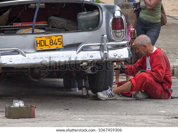 Havana, Cuba - July\
2 2013: A man repairs his classic car in Havana, Cuba. The Cuban\
people are resilient and a lot of cars will have parts from various\
makes and models in\
them