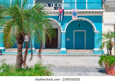 Havana, Cuba July 21 2022: Small Green Palm Tree In Foreground With A Old Architecture On The Background And A Cuban Flag.