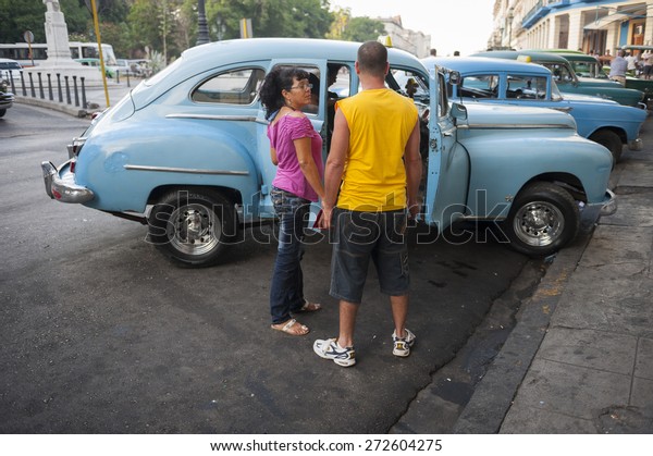 HAVANA,\
CUBA - JUNE, 2011: Cuban passengers wait to enter a classic\
American taxi on the Prado in Central\
Havana.