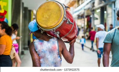 Havana, Cuba. Man Walks Down The Street Carrying His Drum On His Shoulder.  Close Up View From Behind.