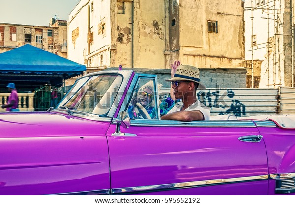 Havana, Cuba -March 14, 2016: Taxi driver in a\
traditional hat driving a vintage American car on Malecon - the\
main promenade in Old Havana,\
Cuba.