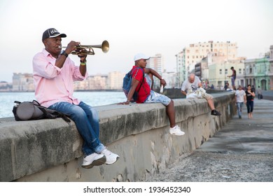 HAVANA, CUBA - MARCH 2, 2021: An Older Man, Sitting On The Malecon Wall In Havana, Plays The Trumpet