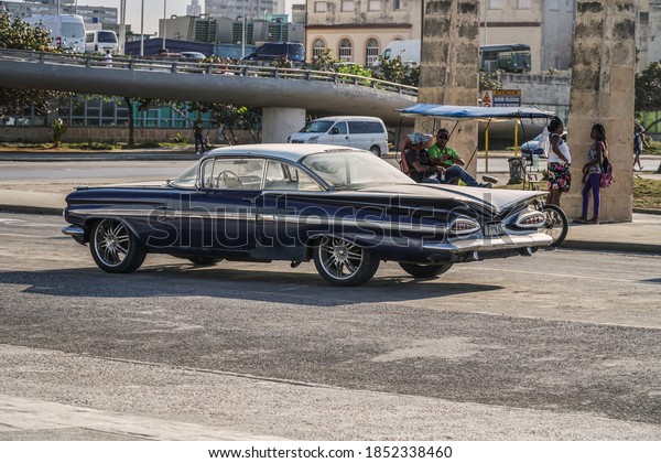           \
HAVANA, CUBA - MARCH 2019: Cuban cars on the street in Havana city.\
Old buildings in Havana and people walking and chatting on the\
street.                 