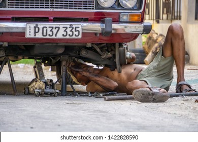 Havana, Cuba - May 17, 2019: Dirty Cuban Car Mechanic is working underneath the vehicle in the streets of Old Havana City during a hot sunny day.