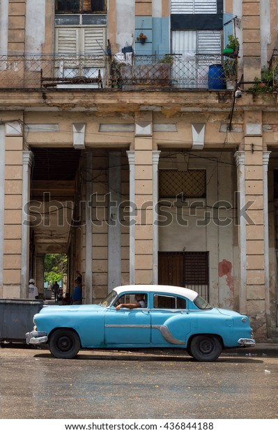 Havana, Cuba - May 28, 2014: Blue\
cuban car and passing by a colonial building in Old\
Havana