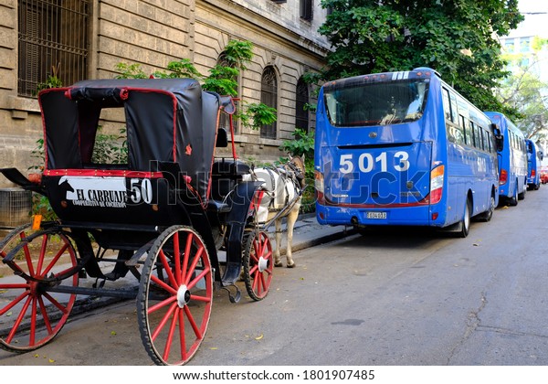 Havana, Cuba - October 2019 : A horse carriage for\
hire parking on a side street behind a row of modern tourist buses\
in downtown Havana,\
Cuba.