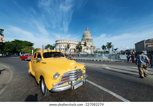 HAVANA, CUBA - OCTOBER 8, 2014: Old classic American\
yellow car rides in front of the Capitol. Before a new law issued\
on October 2011, Cubans could only trade cars that were on the road\
before 1959. 