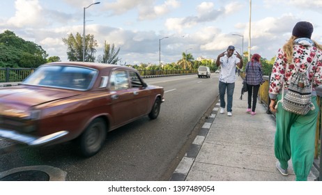 Havana, Cuba-December 2017: Sudden Shot From The Bridge, Where There Is A Cuban Man Posing For The Camera And Cuban Car Passing Fast Next To Him On The Driveway. Vibrant City Of Havana. Lifestyle.  