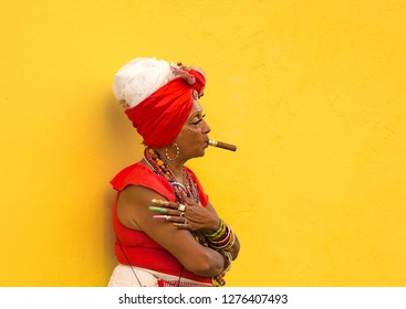 HAVANA-CUBA- DEC 4, 2018:  Woman with a cigar in her mouth with a yellow background letting tourists take photos of her for a few pesos in Havana street in Cuba