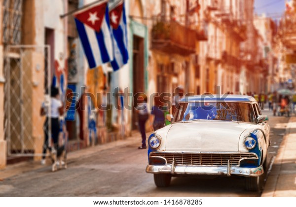 HAVANA,CUBA - JUNE 5,2019 : Cuban\
flags, classic car and colorful decaying buildings in Old\
Havana