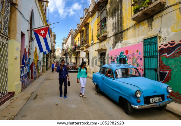 HAVANA,CUBA - MARCH\
16,2018 : Street scene with cuban flags, old car and colorful aged\
buildings in Old\
Havana