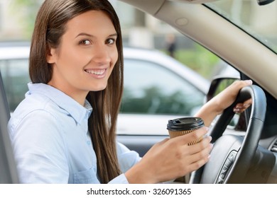 Have a break. Agreeable  charming   happy  delighted woman drinking coffee and sitting at the wheel while driving a car  - Shutterstock ID 326091365
