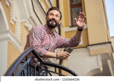 Have A Good Day. Low Angle Of Joyful Bearded Man Standing On The Porch And Greeting His Neighbour